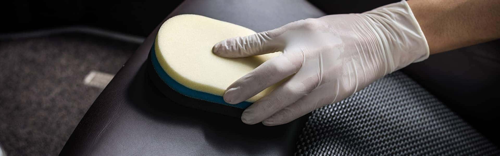 A person cleaning a leather car seat with a sponge