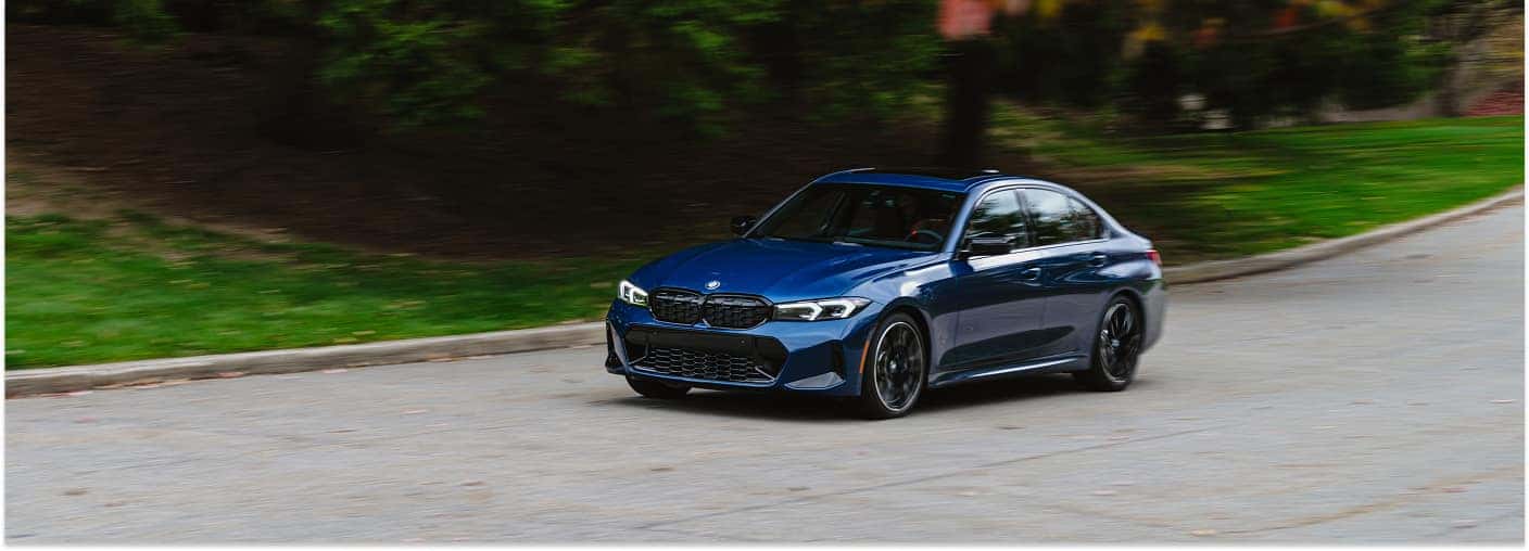 Blue 2026 BMW 3 Series sedan driving on a road in front three-quarter view.
