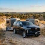 2026 Cadillac Escalade, in a sophisticated dark metallic finish, is positioned confidently on a wide, unpaved ranch road in lampasas texas