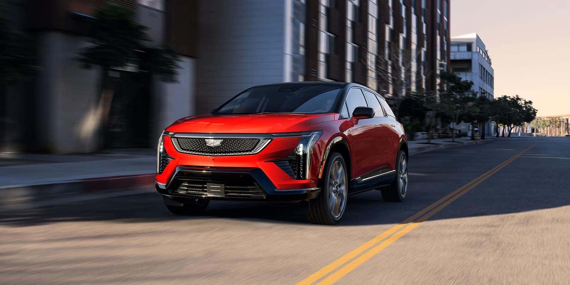 2027 Cadillac OPTIQ in red, front driver-side view in city traffic, at Covert Cadillac Bee Cave in Austin