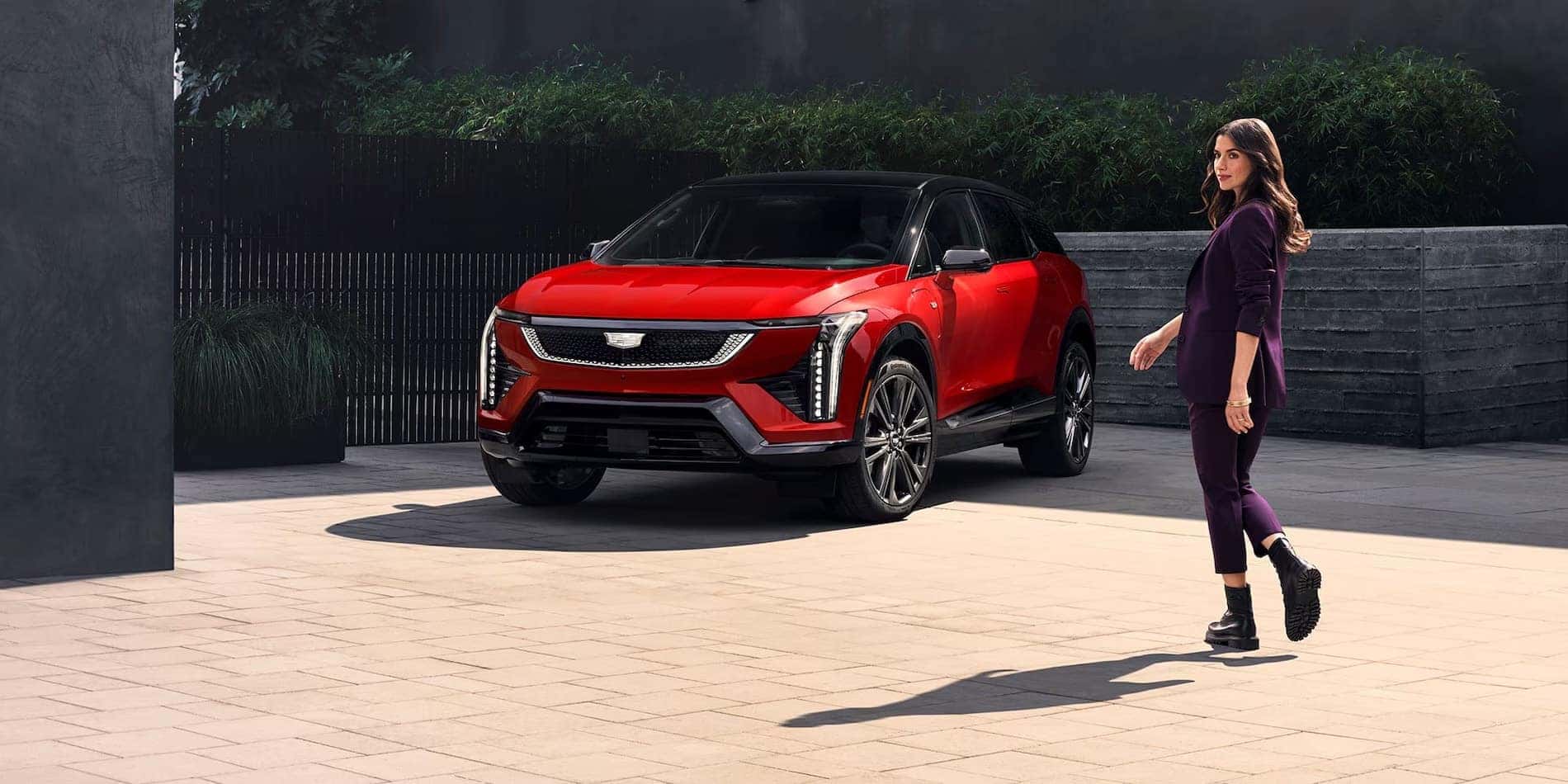 2027 Cadillac OPTIQ in red, front passenger side, with owner alongside, at Covert Cadillac Bee Cave in Austin