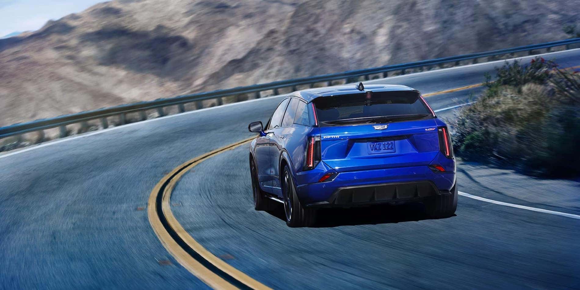 2027 Cadillac OPTIQ-V in blue, rear three-quarter through a curve, at Covert Cadillac Bee Cave in Austin
