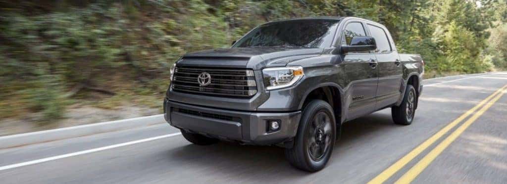 A dark grey 2021 Toyota Tundra with black ascents and black wheels zips around a tight bend on the road.
