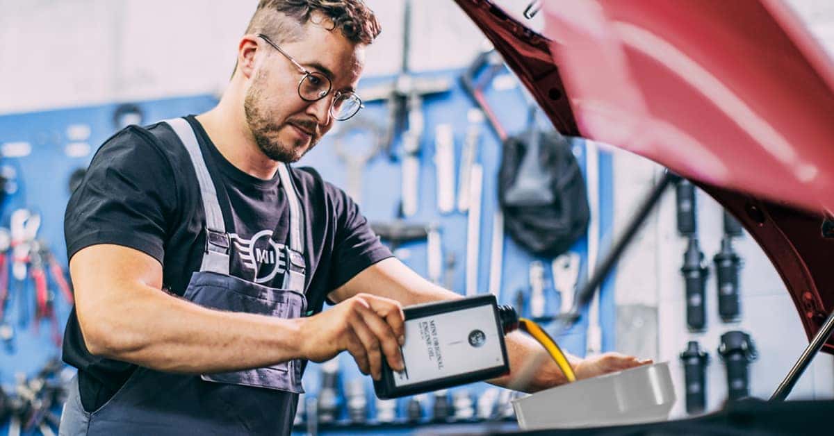 Image shows a MINI service advisor adding oil to a MINI vehicle in a garage.