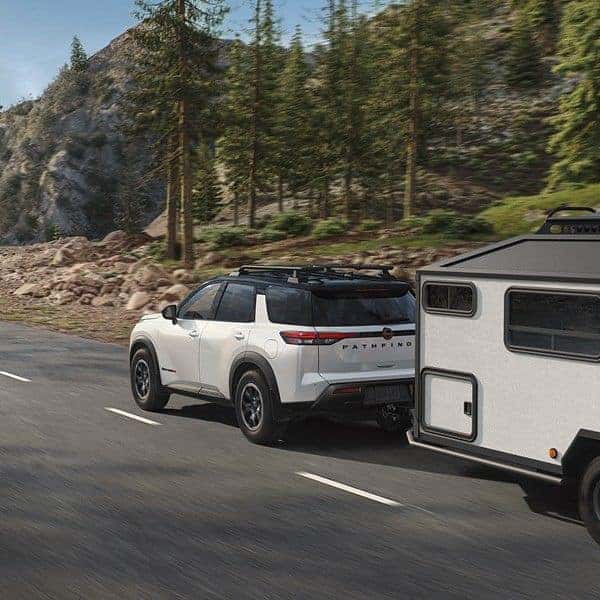 2026 Nissan Pathfinder SUV towing a travel trailer on a mountain road, showcasing capability & versatility in St. George, UT