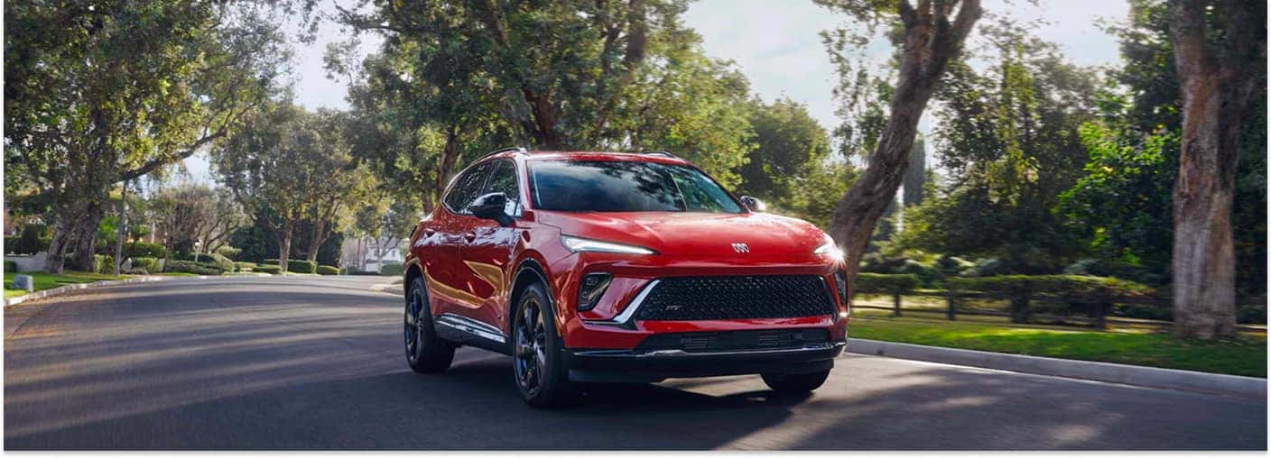Front three-quarter view of a red 2026 Buick Envision SUV driving down a tree-lined street.