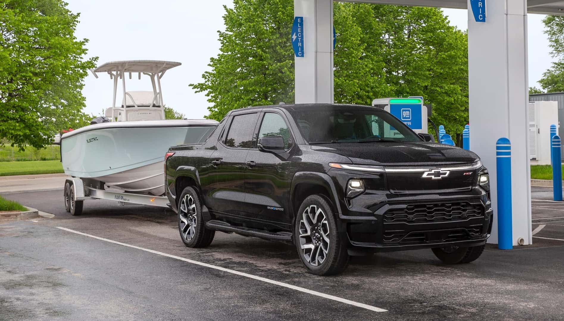 Black 2024 Chevrolet Silverado EV RST at charging station towing a boat