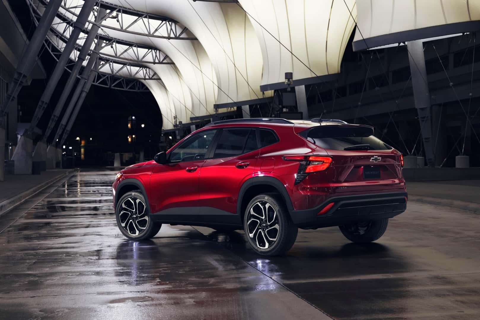 The Safe And Secure 2024 Chevrolet Trax's Sexy Red Exterior, Parked On A Wet Road With The Car's Rear Toward The Camera