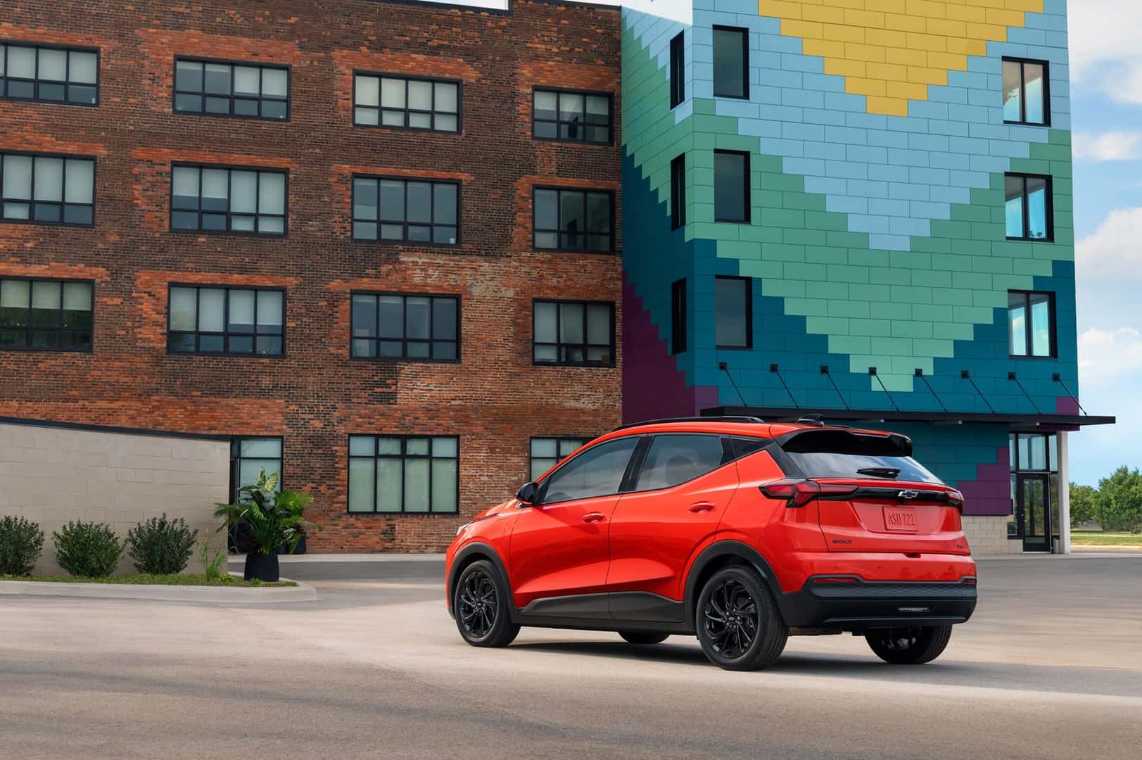 The New And Improved Exterior Of The Technologically Advanced Chevrolet Bolt, Parked Outside A Brick Building With A Gorgeous Mural