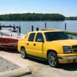 A Sturdy And Strong Yellow Vehicle Backing The Boat and Its Trailer Down The Ramp Into The Lake's Water