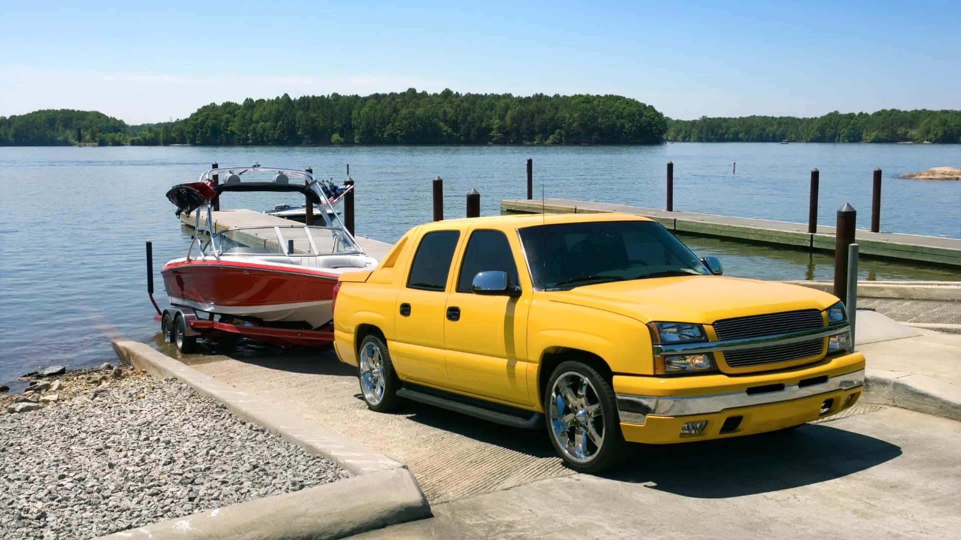 A Sturdy And Strong Yellow Vehicle Backing The Boat and Its Trailer Down The Ramp Into The Lake's Water