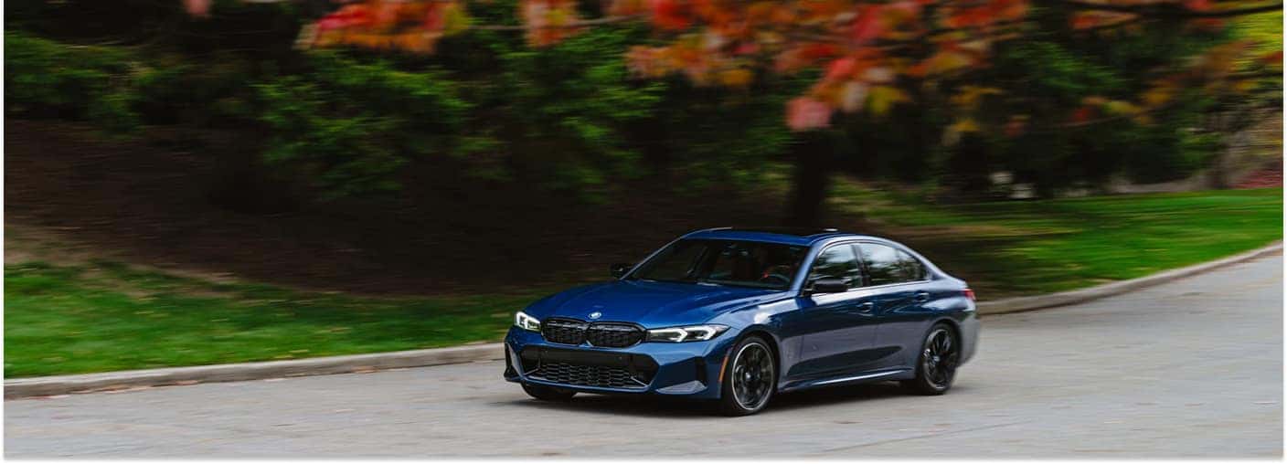 Blue 2026 BMW 3 Series Driving On Road Alongside The Trees