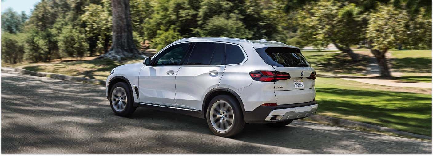 White 2026 BMW X5 SUV in motion on a paved road, rear three-quarter view.