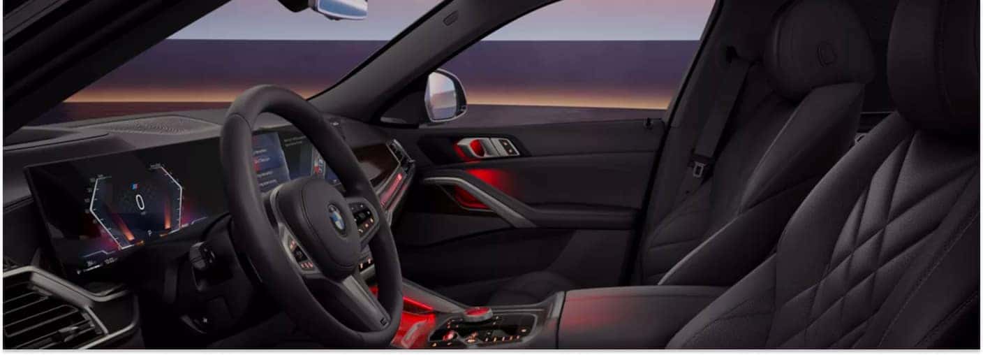 Front interior view of a 2026 BMW X6 featuring black leather seats, curved digital display, and red ambient lighting.